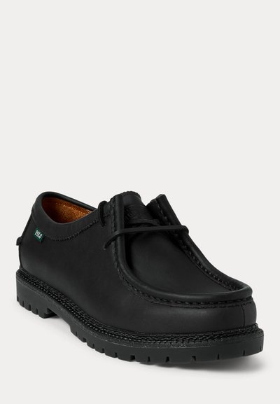 Pantof de piele neagră, în stil mocasin, cu talpă groasă și striată, detalii cusute, șireturi și o mică etichetă verde din material cu inscripția „Polo” pe lateral.