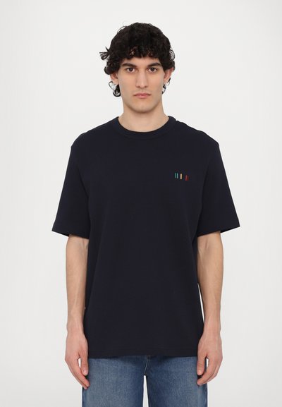 T-shirt en coton marine à manches courtes, avec un col rond et des rayures verticales colorées sur la poitrine gauche. Coupe décontractée avec une texture lisse.