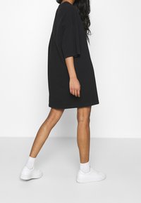 Svart oversized t-shirtklänning med korta ärmar, lös passform och rund halsringning. Bärs med vita sneakers och ankelsockor.