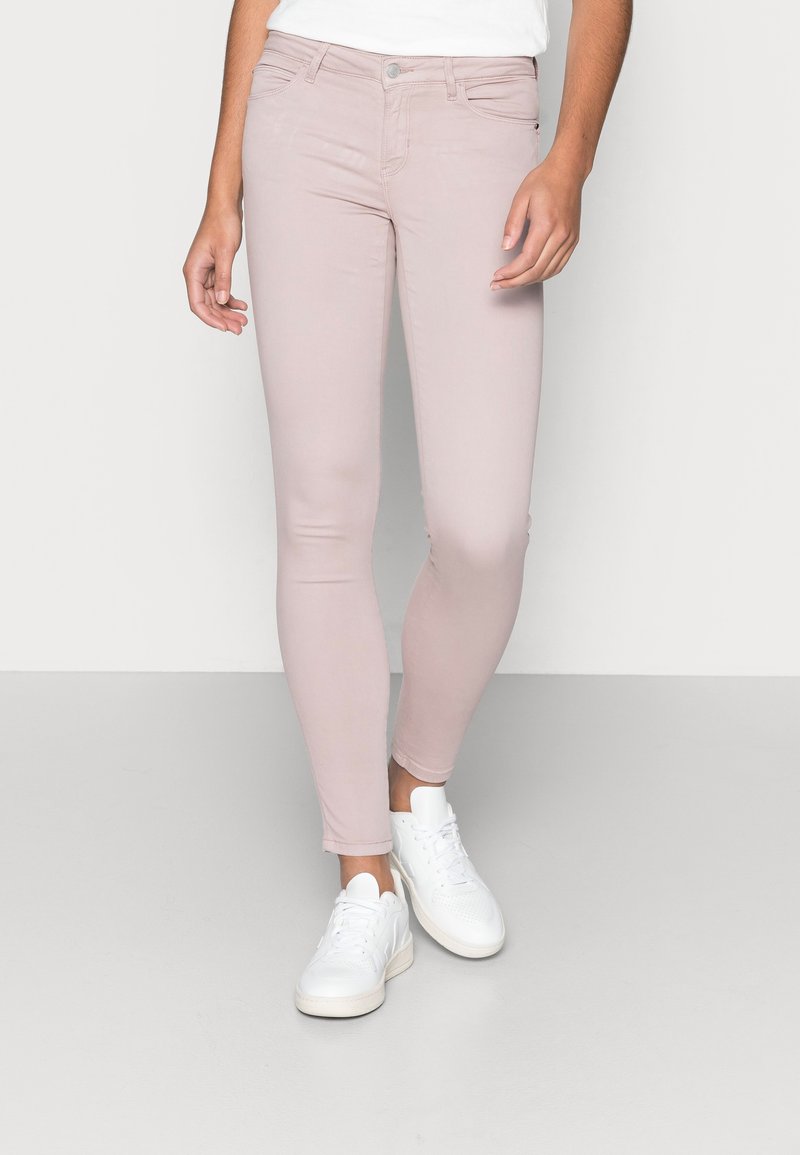 Ljust rosa skinny jeans med en mjuk textur, femfickorsdesign och knappstängning fram, i kombination med vita sneakers.