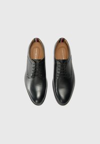 Zapatos de vestir de cuero negro con una textura suave, punta redonda y diseño de cordones de cinco ojales. Incluye un acento interior en contraste.