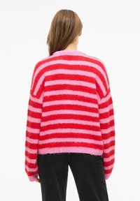 Czerwony i różowy sweter w paski, o luźnym kroju i teksturowanym, puszystym materiale. Posiada szerokie, długie rękawy oraz lekko skrócony dół.