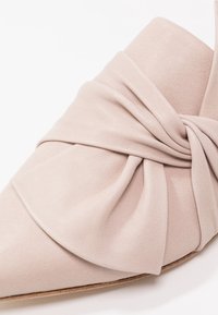 Chaussure en cuir beige à bout pointu avec un grand détail en nœud plissé sur la partie supérieure avant.