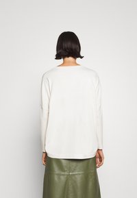 Pull couleur crème avec épaules tombantes, coupe décontractée, col côtelé et texture lisse, associé à une jupe en cuir verte.