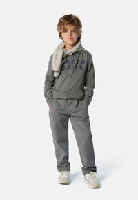 Sudadera gris de manga larga con "NORTH SAILS" impreso en azul marino, bufanda gris clara, pantalones grises y zapatillas blancas con detalles en beige.