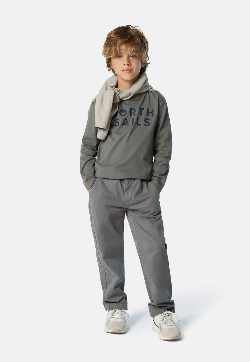 Sudadera gris de manga larga con "NORTH SAILS" impreso en azul marino, bufanda gris clara, pantalones grises y zapatillas blancas con detalles en beige.