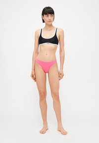 Svart bikini-overdel med hvit kant, parret med rosa bikini-bunn. Materialet ser glatt og elastisk ut, designet for komfort og passform.