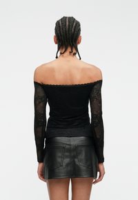 Top negru cu umărul descoperit, cu mâneci lungi din dantelă, având un model floral și un design ajustat, asortat cu o fustă mini din piele neagră.