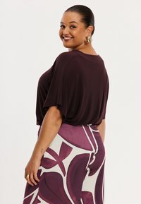 Losse bordeauxrode top met korte mouwen, gecombineerd met hooggetailleerde broek met gedurfde paarse en witte bladpatronen.