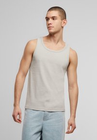 Lys grå tanktop lavet af bomuld, med rund hals og ærmeløs design. Stoffet har en glat tekstur med subtil ribbning.
