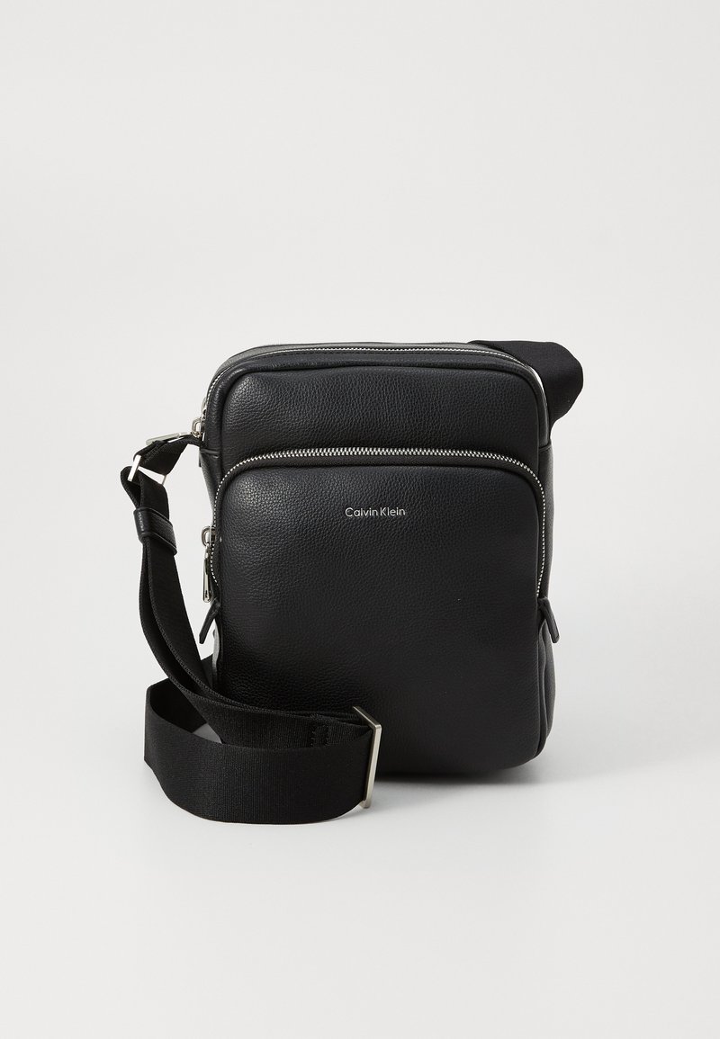 Sort Calvin Klein crossover taske med en lynlåslomme og justerbar rem, placeret mod en neutral baggrund.