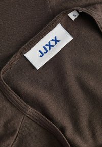Vêtement en mélange de coton marron avec une texture lisse, doté d'un col et d'une étiquette avec "JJXX" imprimé en bleu et taille "S".