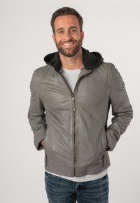 Grijze leren jas met een zwarte capuchon, rits aan de voorkant, zijzakken en gestikte accenten. Draagt over een wit t-shirt en blauwe jeans.