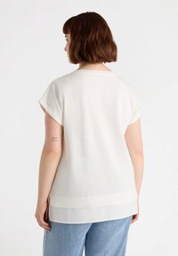 Top blanco de manga corta con un corte relajado. Textura suave y sutiles capas en el dobladillo. La vista trasera revela un diseño simple.