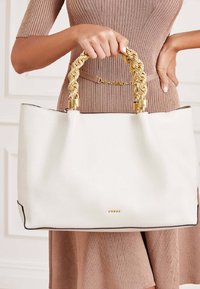 Sac cabas en cuir blanc avec une finition texturée et des poignées tressées en or. Comprend des accents de quincaillerie dorée et une bordure contrastante noire.