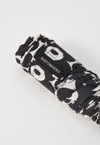 Mustvalge mustriga kompaktne vihmavari, millel on kangakate. Omab korrapärast rullitud disaini ja nähtavat brändimärki, millel on kiri "marimekko."