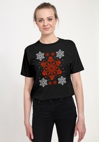 Černé tričko s krátkým rukávem, které má živý červený a bílý vzor sněhových vloček se skull motivy ve středu a kolem.