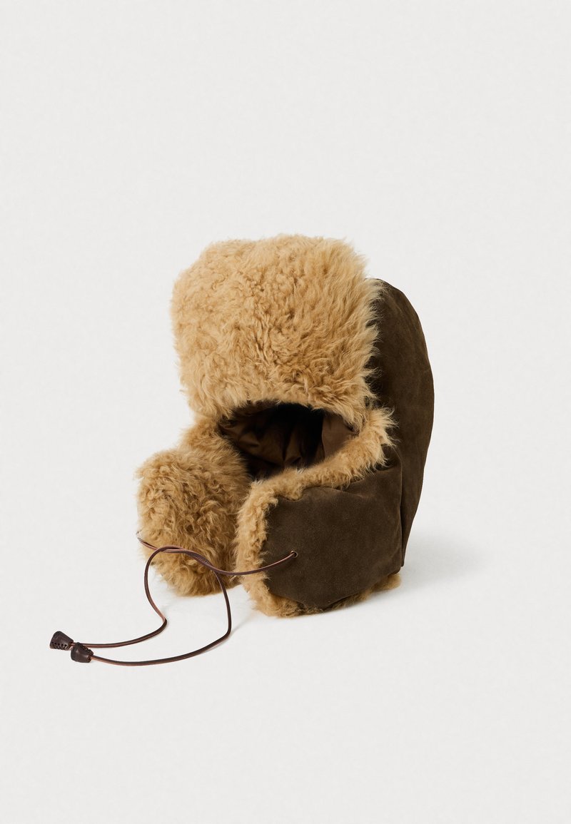 Pălărie din suede maro, căptușită cu blană de miel, cu un tiv pufos de culoare bej, având un sistem de închidere cu șnur și un design rotund.