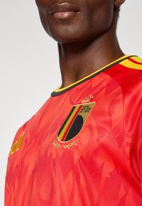Close-up van een persoon die een rood shirt van het Belgisch nationaal voetbalteam draagt met het embleem van de Koninklijke Belgische Voetbalbond op de borst.