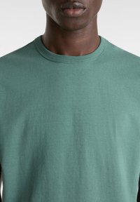 Grünes Baumwoll-T-Shirt mit Rundhalsausschnitt, glatter Textur und lässiger Passform, ohne sichtbare Muster oder Akzente.