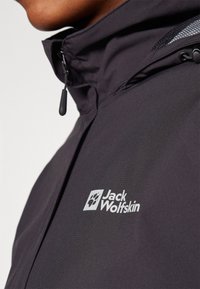 Black jacket with matte finish, featuring a high collar and logo. Zipper detail visible, with a smooth texture and streamlined design.