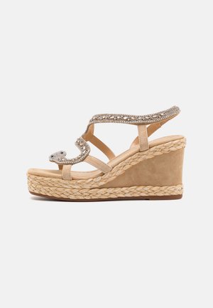 Sandalo con zeppa beige caratterizzato da una parte superiore in suede liscia, dettagli metallici, una piattaforma in juta intrecciata e un design open toe.
