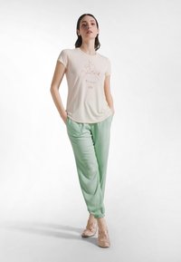 Kremowy T-shirt z krótkim rękawem z grafiką góry, zestawiony z jasnooliwkowymi, luźnymi spodniami dresowymi i jasnoróżowymi baletkami.