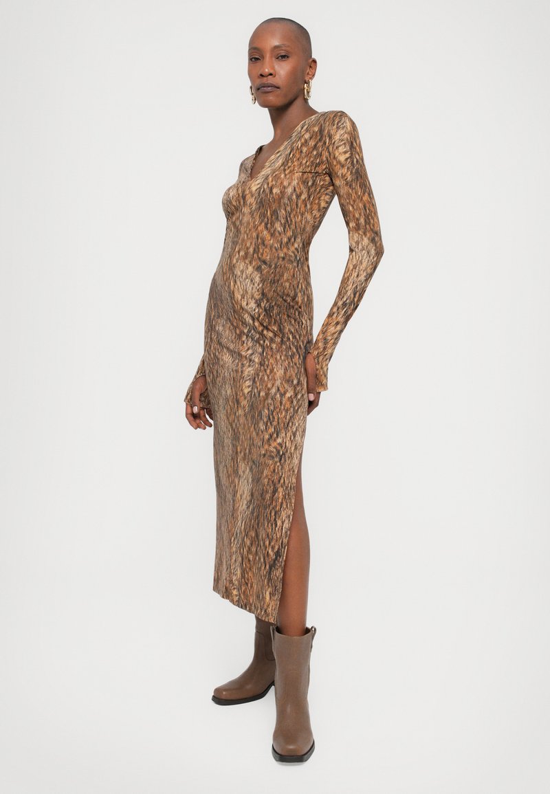 Långärmad brun klänning med v-ringning, figurnära silhuett och abstrakt texturmönster, kombinerad med bruna ankelstövlar.