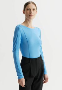 Niebieska bluzka z długim rękawem i okrągłym dekoltem, z kontrastowymi przeszyciami, zestawiona z czarnymi spodniami o wysokim stanie, posiadającymi boczne kieszenie.