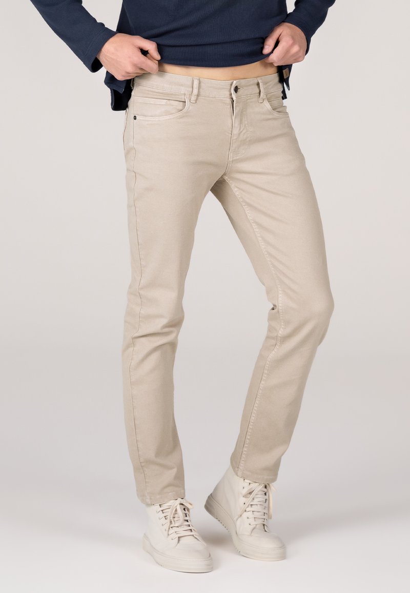 Beige Baumwollhosen mit einem taillierten Design, im fünf-Taschen-Stil und mit einem Knopfverschluss, kombiniert mit weißen High-Top-Sneakern.