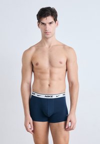 Dunkelblaue Nike-Boxershorts mit einem weißen elastischen Bund, der ein schwarzes Logo trägt. Glatte Stofftextur und formschlüssiges Design.