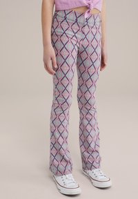 Izplešušas bikses purpurā, tirkīza un baltā ģeometriskā dimanta rakstā, izgatavotas no elastīga auduma, apvienotas ar baltām sporta kedām.