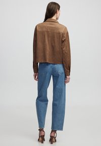 Bruine suède cropped jack met een kraag, lange mouwen en een gladde textuur, gecombineerd met lichtblauwe high-waisted denim jeans.