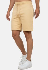 Pantaloni corti beige realizzati in tessuto morbido, con vita elastica e cordino. Presentano tasche laterali e una sottile ricamo del logo sull'orlo.