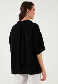 Black oversized short-sleeve shirt with a subtle textured pattern. Features a classic collar and straight hem.