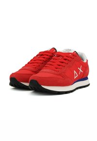 Sneaker rosse in suede con una suola intermedia bianca, suola in gomma nera e accento blu. Caratteristiche includono lacci rotondi e design geometrico.