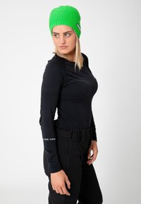 Black long-sleeve shirt and black pants, paired with a bright green knit beanie featuring a logo patch on the front.