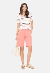 Korte mouw gestreepte T-shirt in wit, roze en marineblauw; koraal kleurige knielange shorts; lichtbeige tas; tan sandalen met een enkele band.