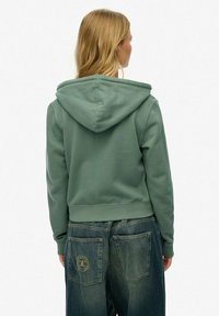 Groene katoenen hoodie met een trekkoordkap en een verkort zoom, gecombineerd met losse blauwe jeans met grote achterzakken en logo detail.