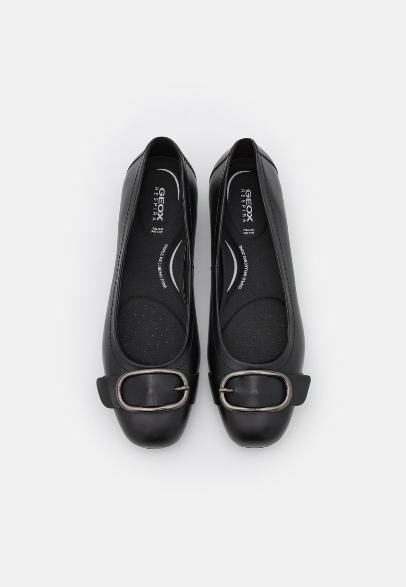 Des ballerines noires en matériau lisse avec un bout arrondi, présentant un détail de boucle en métal sur une large sangle et une semelle intérieure rembourrée.