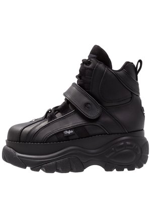 Black high-top sneakers with a thick rubber sole, leather upper, lace and Velcro strap closures, and textured side panel detailing.