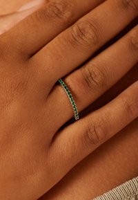 Groene stenen bandring gedragen aan een hand, met een fijn zilveren bandje en een rij kleine smaragdachtige edelstenen, met een gladde textuur.