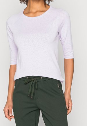 Jasnofioletowa, lekka koszulka z rękawami do łokcia i zaokrąglonym dekoltem, zestawiona z ciemnozielonymi dresami z sznurkiem i zapinanymi na zamek kieszeniami.
