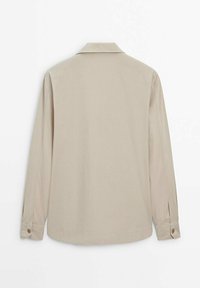 Camicia beige chiaro a maniche lunghe con colletto, polsini abbottonati e un tessuto liscio e testurizzato. Nessun logo o motivo visibile.