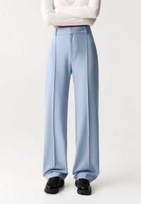 Hellblaue, weit geschnittene Hosen aus glattem Stoff, mit einer vorderen Nahtdetail und hohem Bund. Getragen mit schwarzen Sneakers.