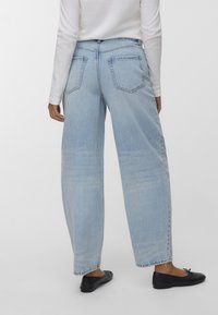 Světle modré džíny s vysokým pasem a volným střihem, s velkými zadními kapsami a mírným vyblednutím. Kombinováno s černými plochými botami.