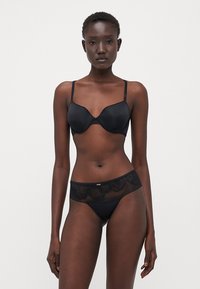 Soutien-gorge noir avec coque moulée et bretelles ajustables, accompagné de culottes noires avec une superposition en dentelle florale transparente et un band élastique.
