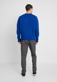 Niebieski sweter z okrągłym dekoltem, o fakturalnym wykończeniu i długich rękawach, zestawiony z szarymi spodniami i czarnymi sneakersami, widziany od tyłu.