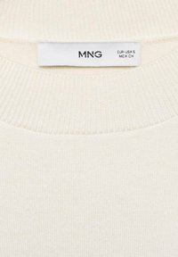 Pull en maille côtelée de couleur crème avec une étiquette blanche indiquant la marque MNG et la taille EUR-USA S MEX CH.