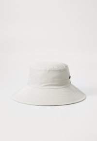 Chapeau seau blanc avec une texture lisse et brillante et un large bord plat. Il présente une bande cousue autour de la couronne. Matériau durable et résistant à l'eau.